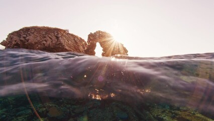 Wall Mural - Splitted underwater footage of the island with limestone arch and coral reef below the surface. Famous Batu Bolong diving spot in Komodo National Park, Indonesia