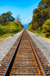 Dead-straight, single-track railroad along the Pacific Coast in Carpinteria, California on a sunny day. The tracks run parallel to the famous Highway 1 from Los Angeles to San Francisco (USA). 