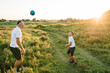 Handsome dad with little cute son playing football on green grass at sunset. Father and young boy playing in field with soccer ball. Concept of having fun and sport. Friendly family. Father's Day.