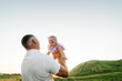 Kid funny with parent in grass field at sunset. Father holds throws up happy daughter plays in nature on summer day. Dad, child walk in mountains. Family spending time together. Girl flies in sky