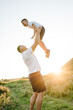 Dad throws up son in sky at sunset. Happy son playing with dad in green grass on field in summer mountains. Kid with parents smiling, spending time together. Children's, Father's Day. Friendly family.