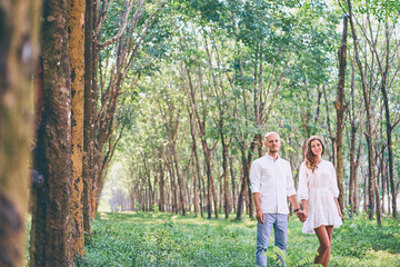 Wall Mural - Romantic couple wearing white cloth walking in green park, having a date.