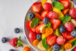 Summer fresh fruit salad in a bowl on white marble background. Top view. Healthy food for breakfast. Mixed strawberries, grapes, banana, kiwi, blueberries, peach, kumquat and mint for diet lunch