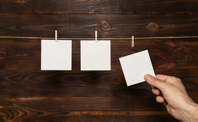Wall Mural - man hand take paper note cards hanging with wooden clip or clothespin on rope string peg on wooden background