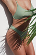 Young Woman in Green Bikini Posing with Palm Leaf on White Background