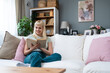Simple living. Portrait of young beautiful blonde student or college girl sitting at home on sofa enjoying her life, free time and new apartment that she rented and moved in to live alone in quiet.