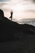 Silhouette woman in yoga pose on rock of the beach at sunset or sunrise.