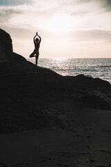 Wall Mural - Silhouette woman in yoga pose on rock of the beach at sunset or sunrise.