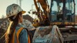 A female construction worker wearing a hard hat and safety vest is standing at a construction site, looking at an excavator.