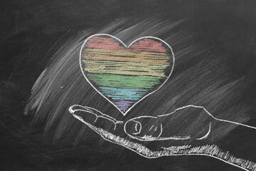 A hand sketches a colorful heart with rainbow chalk stripes on a dark chalkboard background, representing love and diversity. LGBT, pride concept