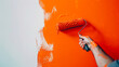 Applying orange paint with a roller on a white wall