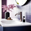 White ceramic vessel sink and brass faucet on white counter mounted on violet tiles wall with mirror. Minimalist interior design of modern bathroom.