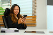 Attractive businesswoman texting messages on smartphone sitting in office
