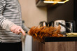 Closeup shot of man dusting kitchen with a feather duster. Housekeeping concept