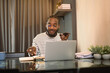 Young stylish African man having phone conversation and working with laptop at home
