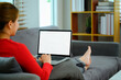 Side view carefree young woman in red sweater using laptop on couch at home