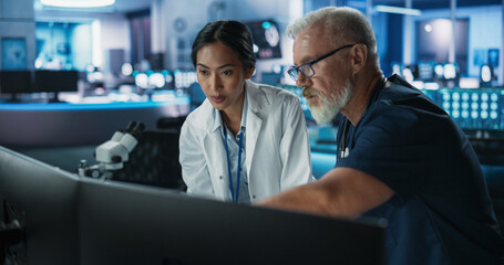Poster - Asian Female Scientist Using Desktop Computer And Talking To Caucasian Male Doctor In Modern Hospital Research Lab. Colleagues Discussing Test Results Of Patients, Treatment Methods, Medication.