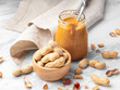 Roasted peanuts in wood bowl and peanut butter in glass jar with napkin on marble table