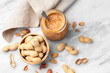 Peanut butter in jar and roasted peanuts with shell in wooden bowl on marble table, top view