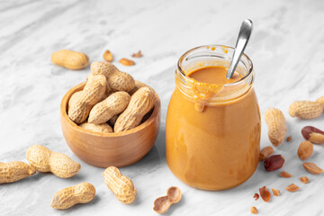 Wall Mural - Peanut butter with spoon in glass jar with peanuts in wood bowl on marble table