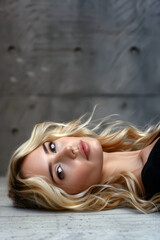 Wall Mural - Beautiful young woman with long blonde hair lies on a concrete floor and stares into the camera.