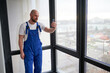 © anatoliy_gleb - Portrait of young bald male construction worker in blue overalls using smartphone. Man standing near big window in apartment under renovation.