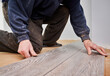 Close up of man construction worker installing laminate timber flooring in apartment under renovation. Male hands placing laminate planks on the floor at home. Flooring renovation concept.