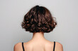© SOLDATOOFF - Back view of young brunette with short curly hair on gray background. Her hairstyle is a bob.