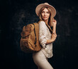 Woman with travel canvas backpack and felt hat on dark background