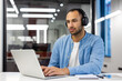 © Tetiana - Concentrated young muslim man working on laptop in modern office, sitting at desk wearing headphones