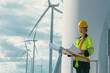 female engineer working outdoor with safety at wind turbines clean energy power station background, worker people with renewable energy technology for future concept.