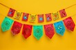 String of handmade cut paper flags isolated on yellow background. Mexican party decoration. Dia de los Muertos, Halloween, Cinco de Mayo. Frame with copy space