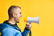 Young angry man shouting and screaming loud holding megaphone