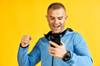 Excited screaming man holding mobile phone over yellow studio background