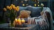 Soft pillows, blanket, burning candles and yellow tulips on rattan garden furniture in evening