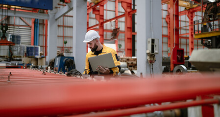 Wall Mural - Industrial engineer in safety helmet uniform jacket working in heavy steel engineering factory. Technician manager worker inspector using laptop in metalwork product manufacturing facility workplace