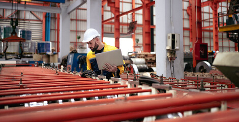 Wall Mural - Industrial engineer in safety helmet uniform jacket working in heavy steel engineering factory. Technician manager worker inspector using laptop in metalwork product manufacturing facility workplace