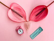 Feminine Health Concept with Menstrual Cup, Birth Control Pills, and Anthurium Flowers on Pink Background.