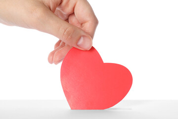 Wall Mural - Woman putting red heart into slot of donation box against white background, closeup