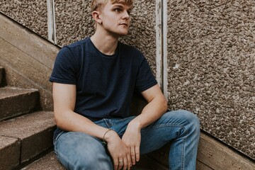 Wall Mural - Blond man in navy blue tee sitting on stairs