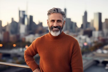 Portrait of a blissful man in his 50s dressed in a warm wool sweater while standing against vibrant city skyline