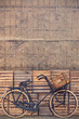 Vintage black cargo transport bicycle with crate carrier in front of old wooden crates and concrete wall
