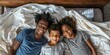 © LukaszDesign - A happy mixed-race family of four in pajamas lying in a row on a bed with a blanket at home. Loveful parents of two. Beautiful girls cuddling with parents before bedtime