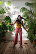Carefree black girl dancing barefoot in headphones listening to music on wooden floor with pleasure, enjoy moment in greenhouse. Relaxed African American woman chilling out to song at home with plants