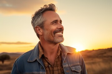 Wall Mural - Portrait of a grinning man in his 50s sporting a versatile denim shirt while standing against vibrant sunset horizon