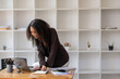 © Wasana - African American businesswoman happily organizing paperwork and using a laptop in a well-lit modern office.
