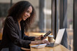 © Wasana - Engaged African American businesswoman working on her laptop while sitting in a sunny café setting.