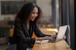© Wasana - Engaged African American businesswoman working on her laptop while sitting in a sunny café setting.