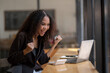 © Wasana - Joyful African American businesswoman celebrating a successful moment while using her laptop in a bustling café.