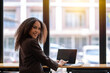© Wasana - Smiling African American businesswoman confidently working on a laptop at a café table with urban background.